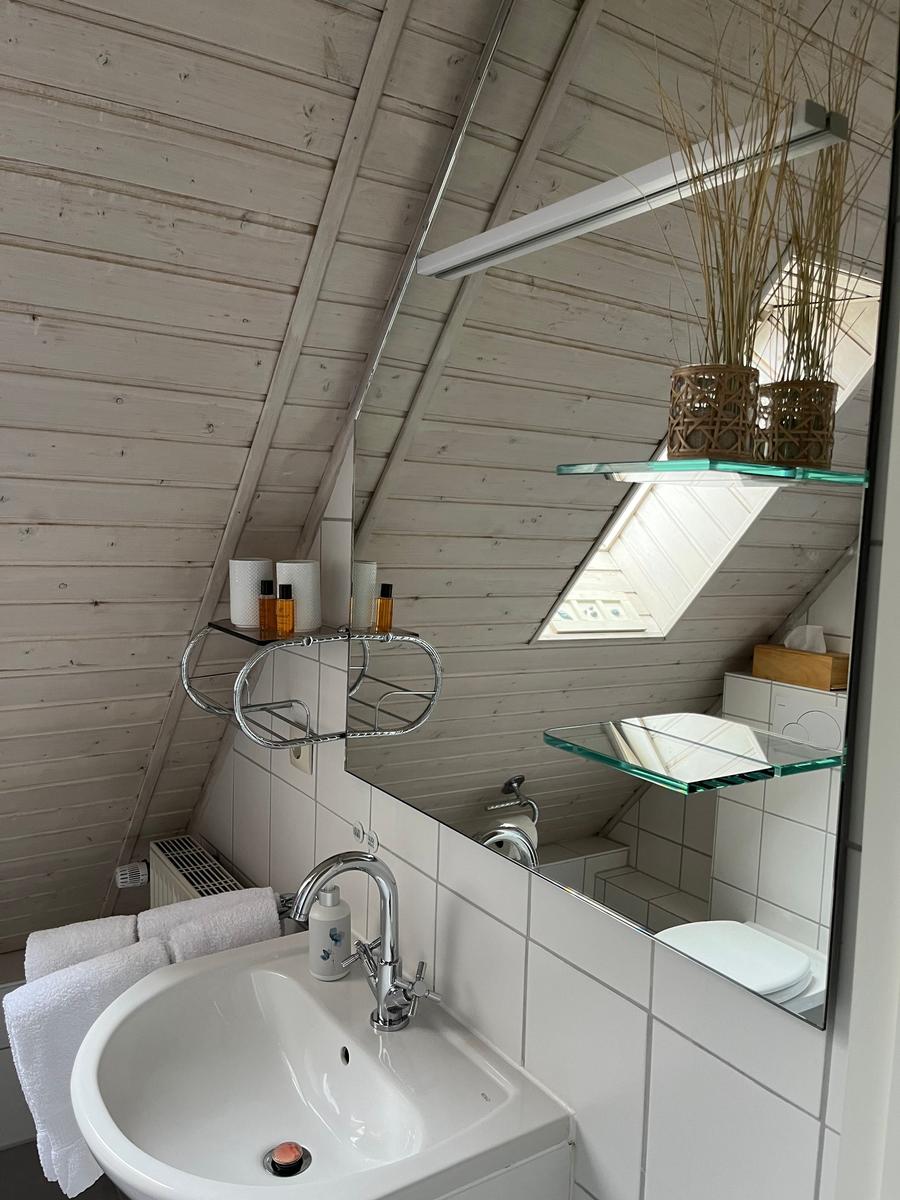 Badezimmer mit Waschbecken, Spiegel und Dachschrägen. Aufbewahrung und Toilette sichtbar.