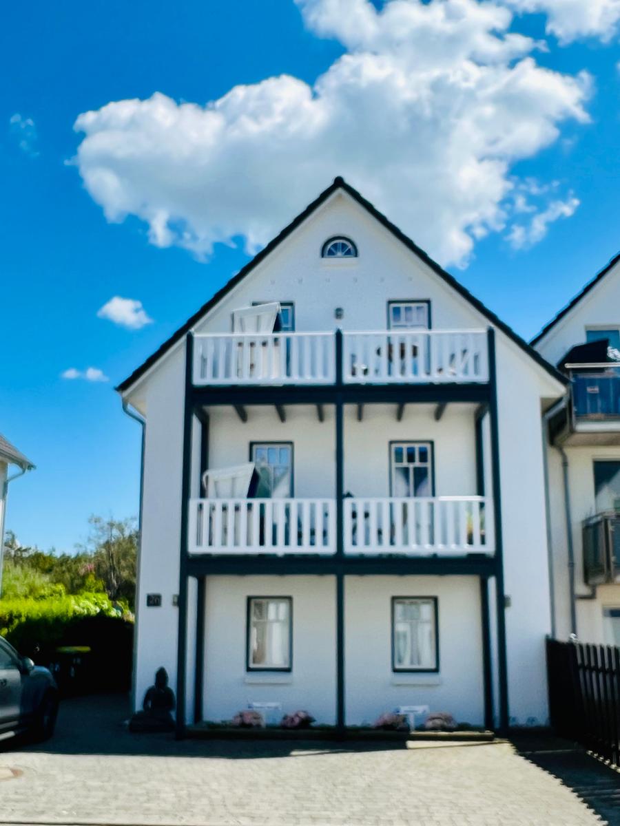 Weiße Hausfassade mit drei Balkonen und Fenstern unter blauem Himmel.
