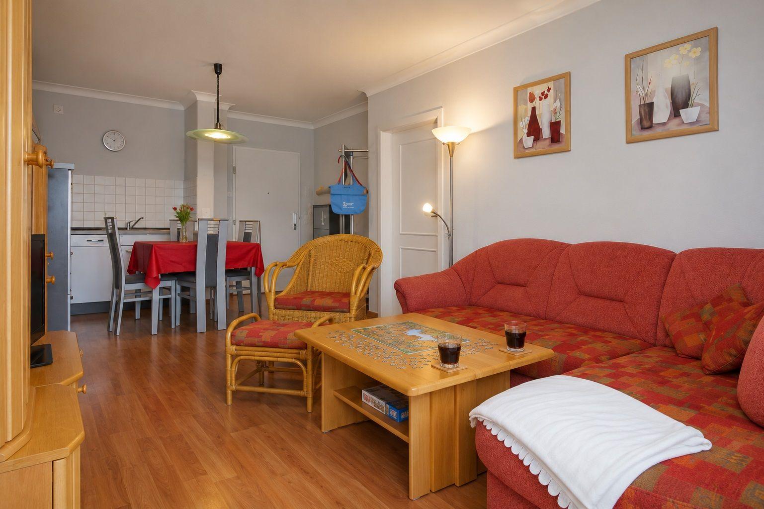 Wohnzimmer mit rotem Sofa, Holztisch und Essbereich im Hintergrund.