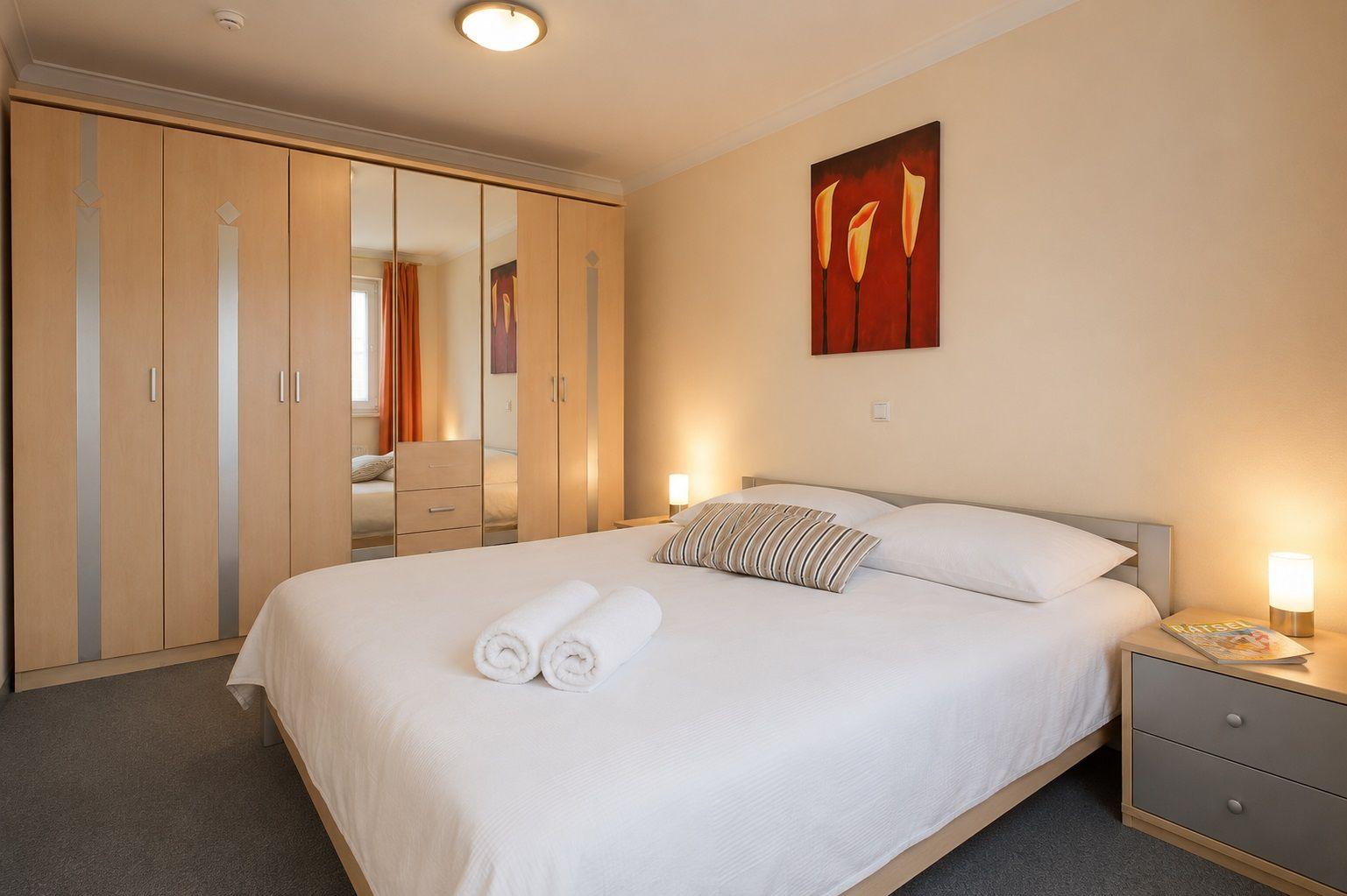 Schlafzimmer mit Doppelbett, Kleiderschrank und Nachttisch. Auf dem Bett liegen zwei Handtücher.