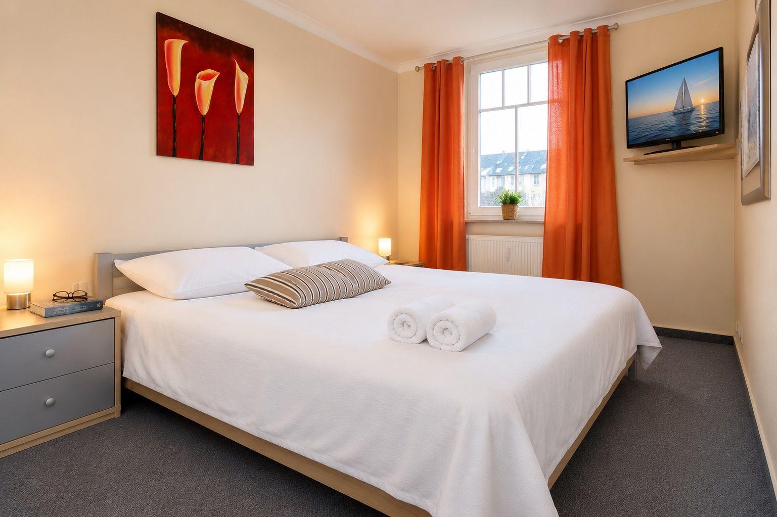 Schlafzimmer mit Bett, Fenster, TV und Wandbild.