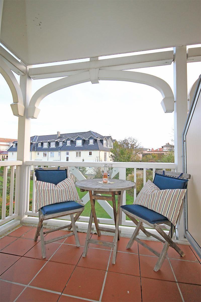Terrasse mit Tisch und zwei Stühlen, Blick auf Wohngebäude und Grünfläche.