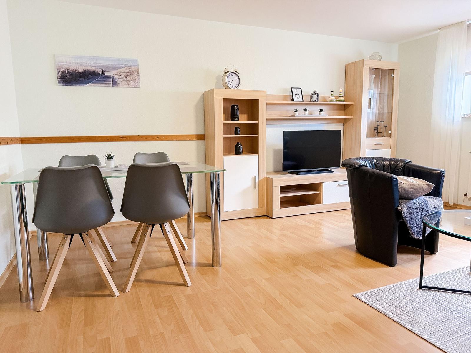 Wohn- und Essbereich mit Esstisch, Sofa, Fernseher und Holzboden.