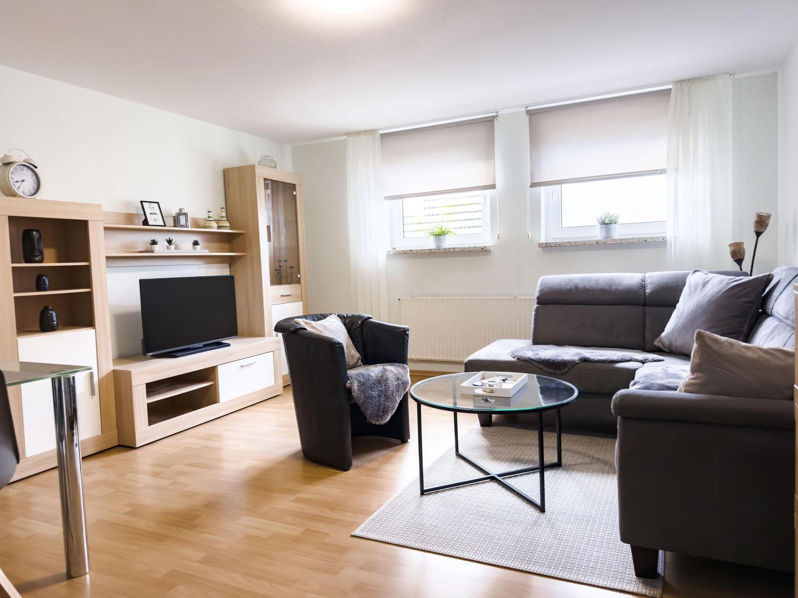 Wohnzimmer mit Sofa, Sessel, Glas-Tisch und Fernseher auf Holzmöbeln.