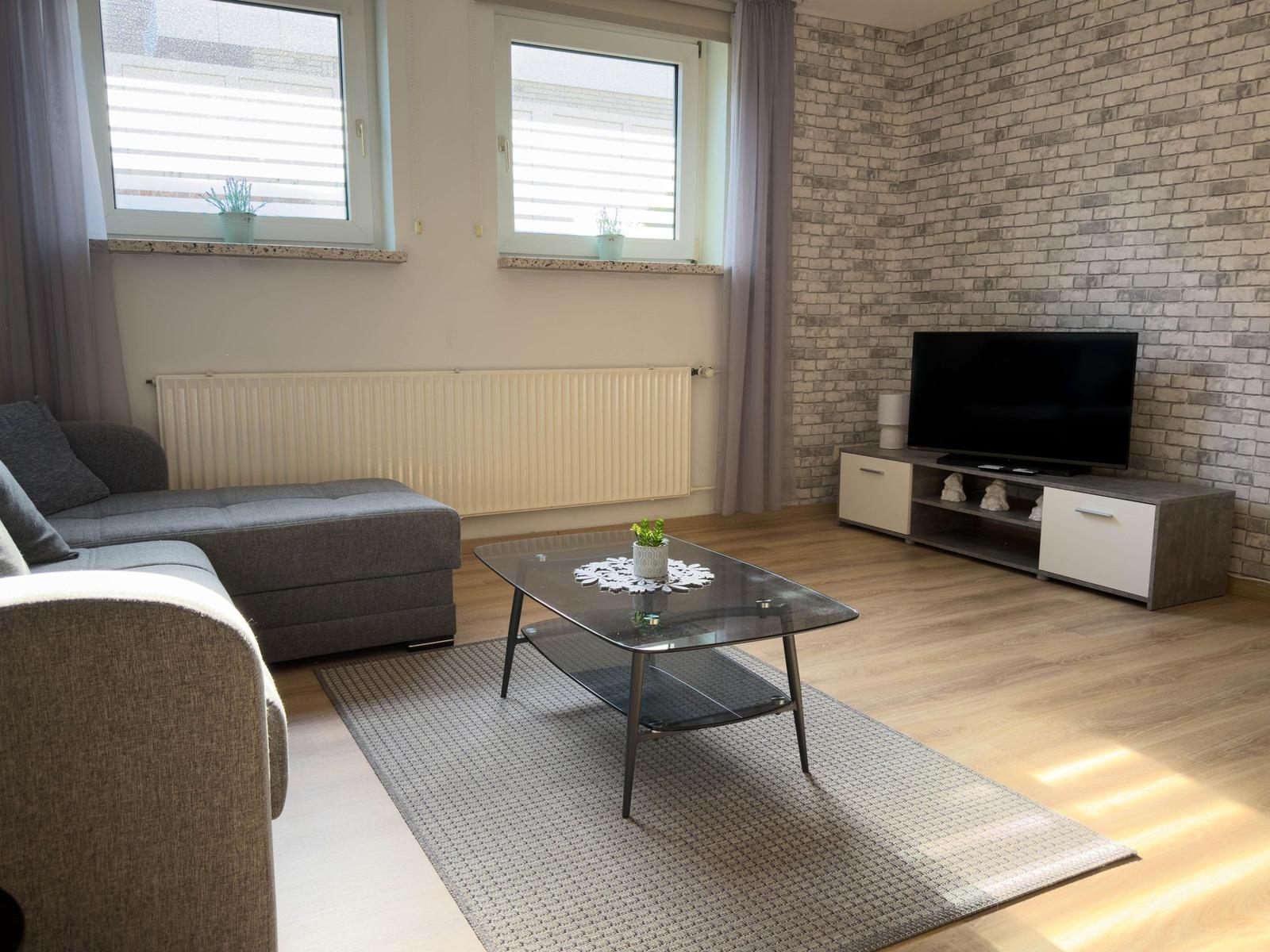 Wohnzimmer mit Sofa, Couchtisch und Fernseher an Ziegelwand.