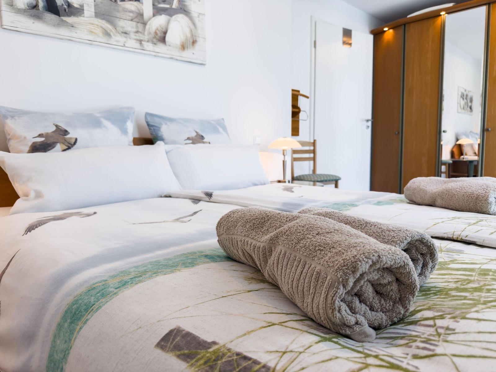 Double bed with patterned bedding and rolled towels. Background: wall art and wardrobe.