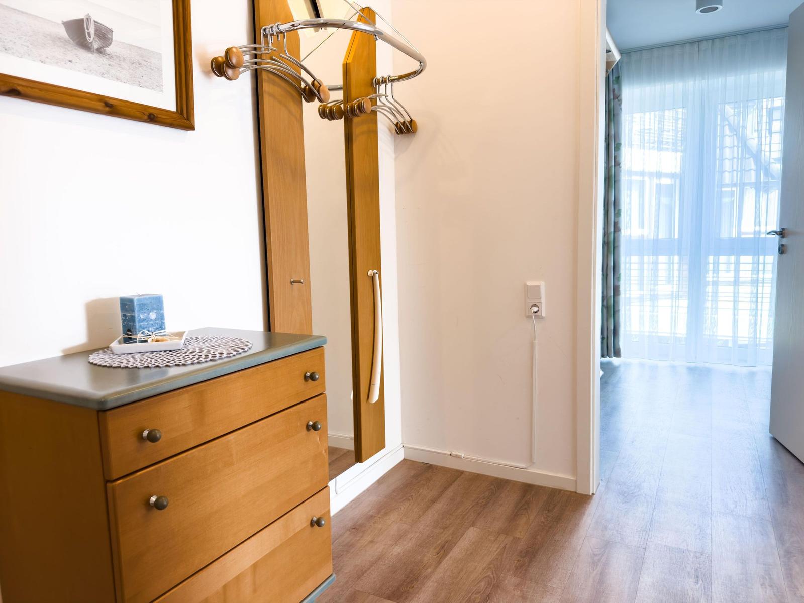 Closet with coat rack and dresser with candle and picture on the wall.