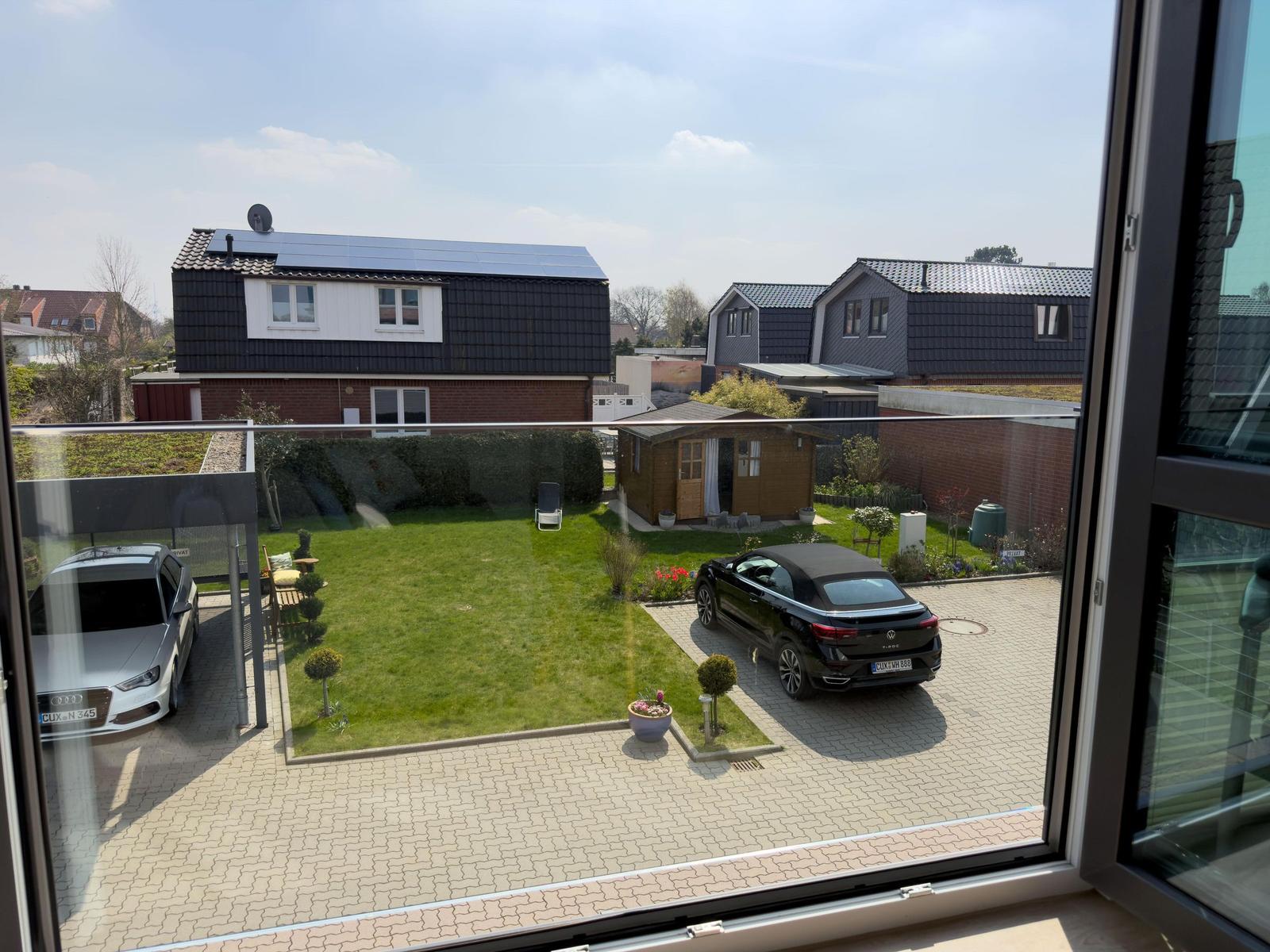 View from window showing paved courtyard, green lawn, and two parked cars.