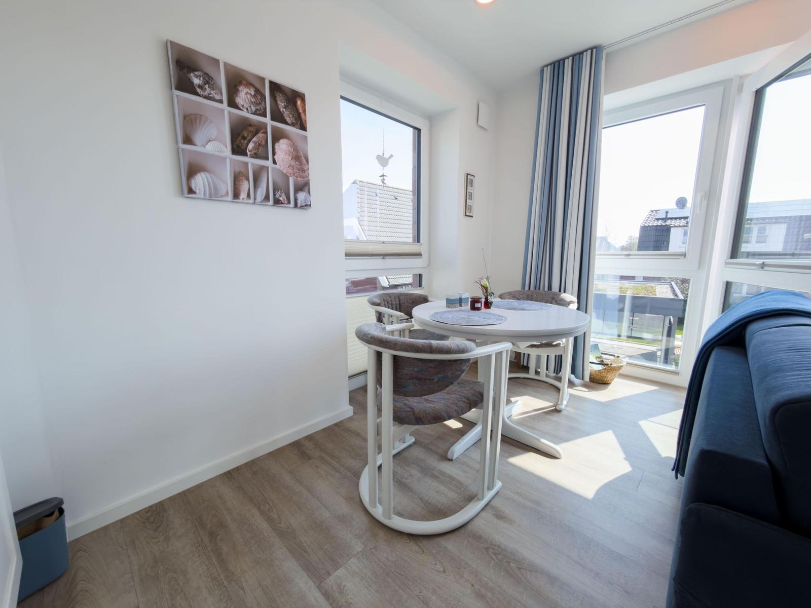 Dining area with round table, three chairs, and window view. Wall art with shells.