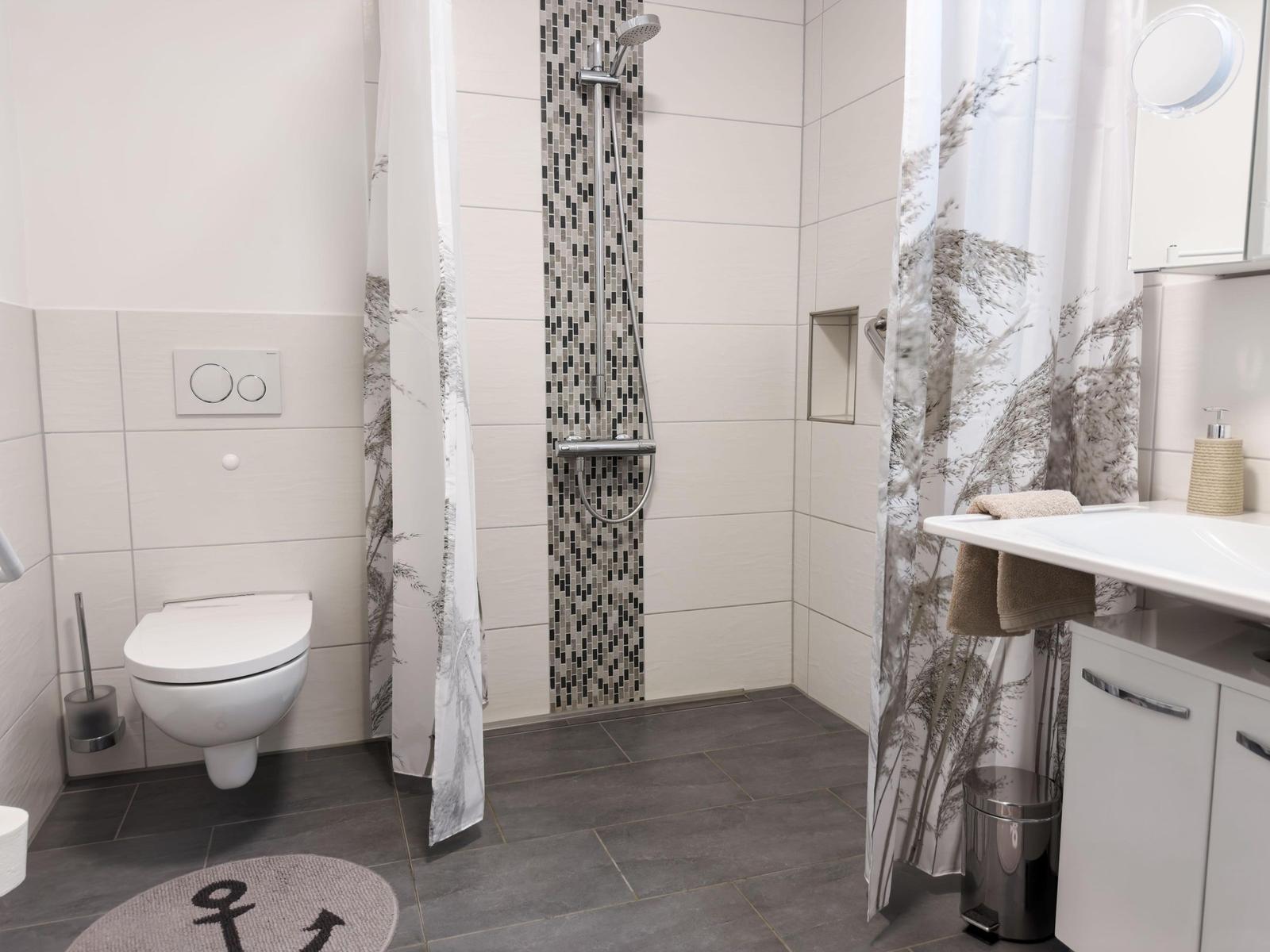 Bathroom with shower, toilet, and sink. Tiles and shower curtain with pattern.