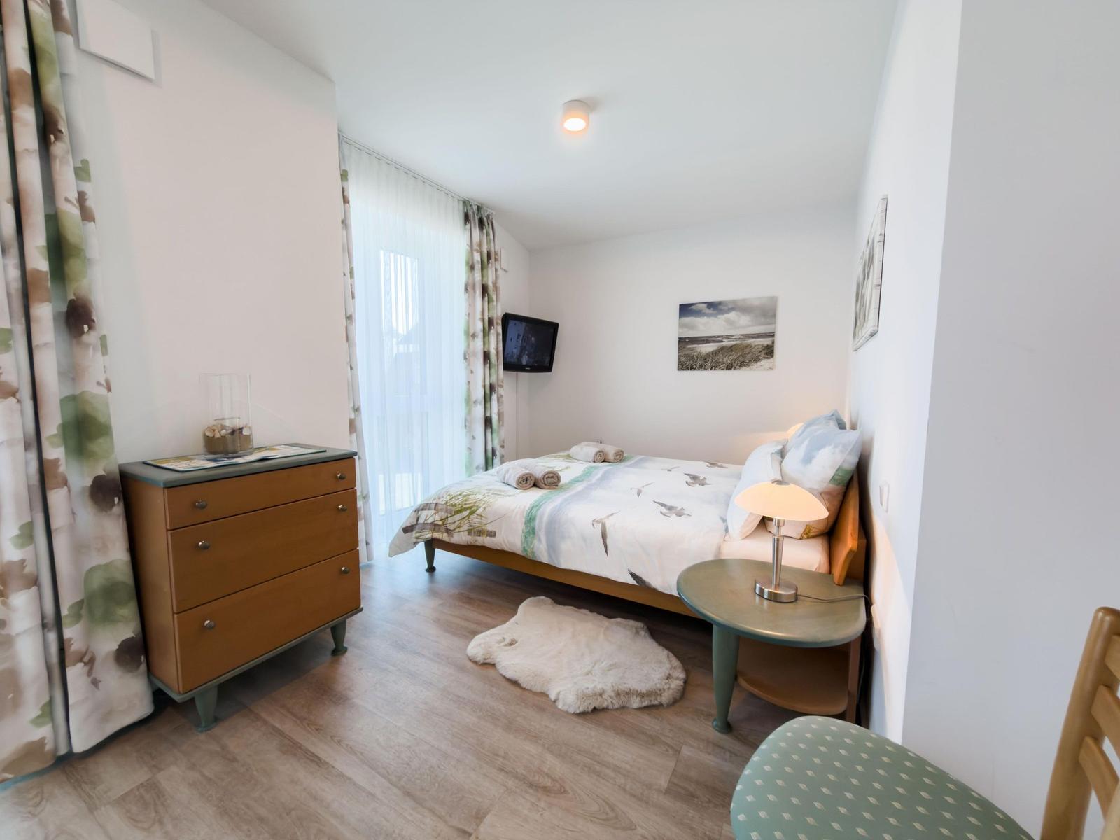 Bedroom with bed, nightstand, dresser, and window with curtains.