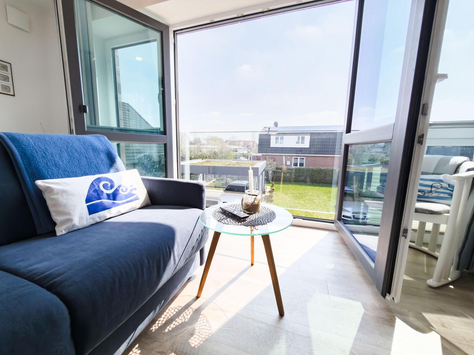 Living area with blue sofa, glass table, and view of a terrace.