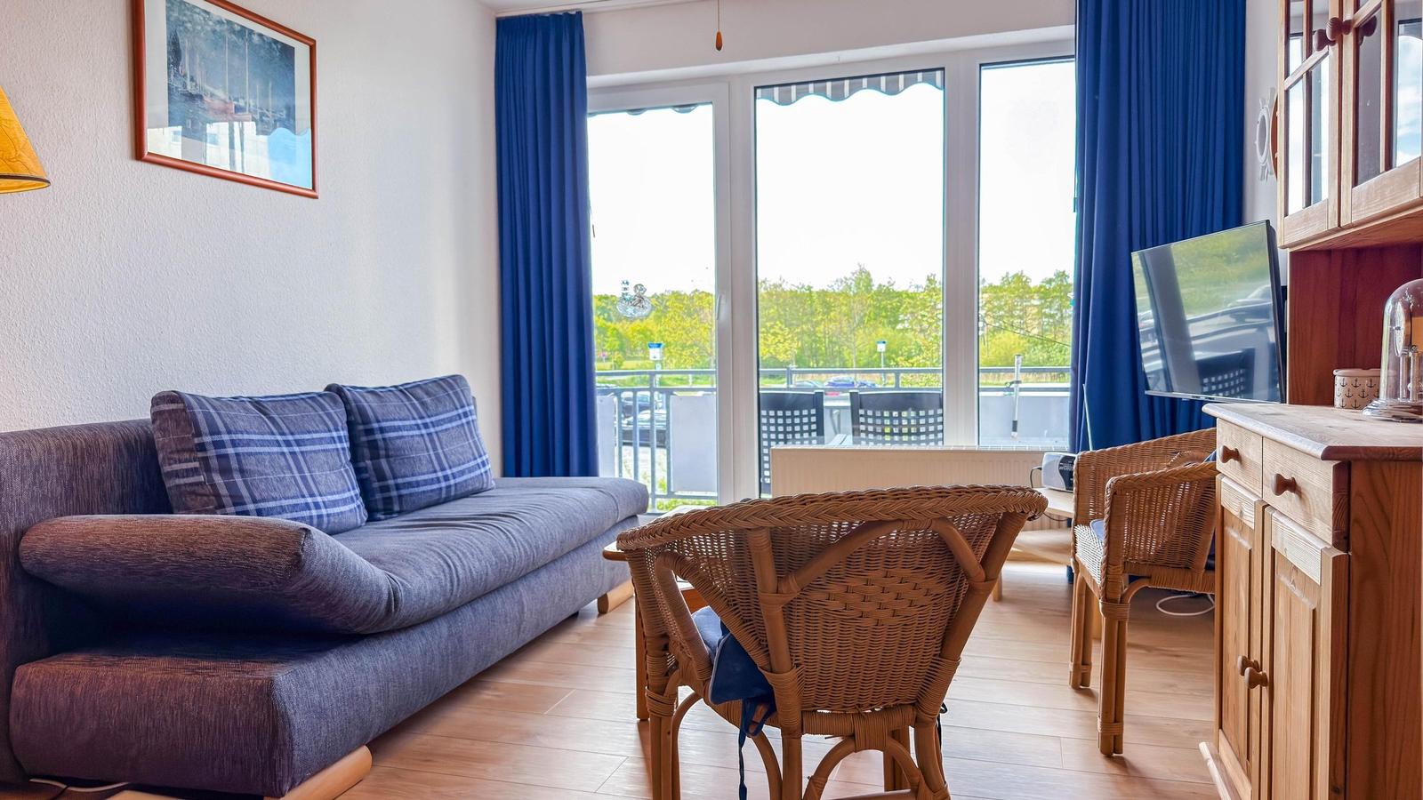 Wohnzimmer mit Sofa, Esstisch und Balkon. Blaue Vorhänge und Holzmöbel.