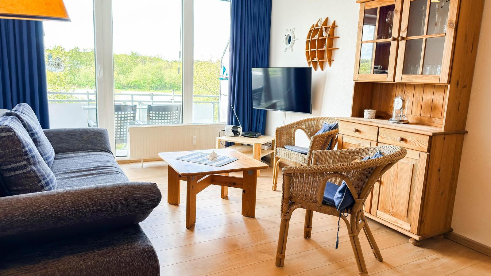 Wohnzimmer mit Sofa, Esstisch, Stühlen und Fernseher. Blick auf Balkon mit Garten.