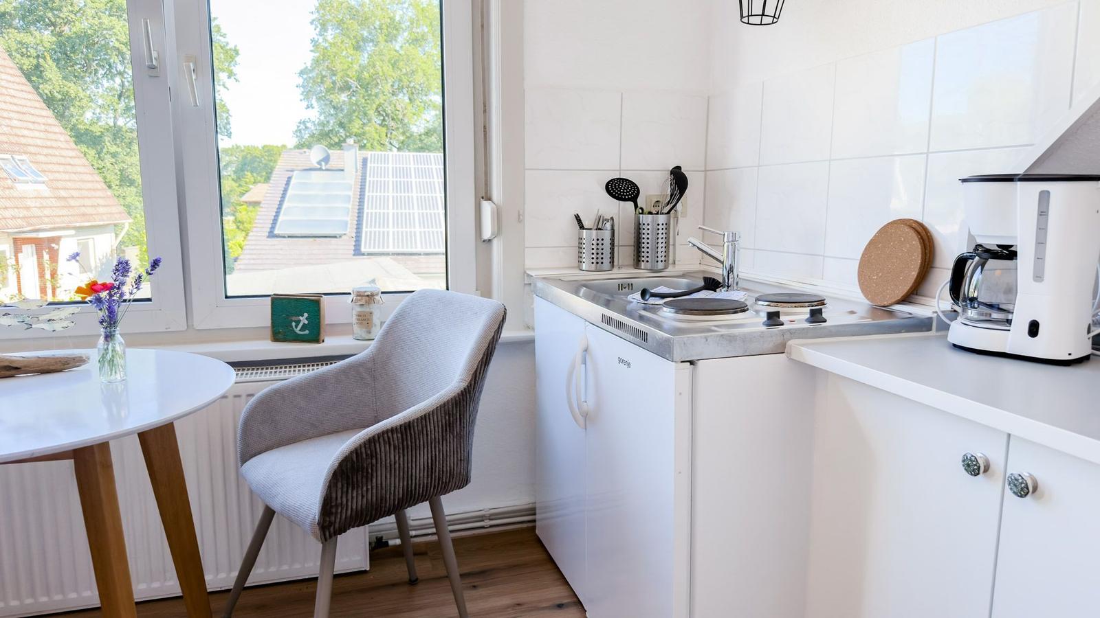 Küche mit Arbeitsfläche, Spüle und Kaffeemaschine. Fenster mit Blick auf Dächer.