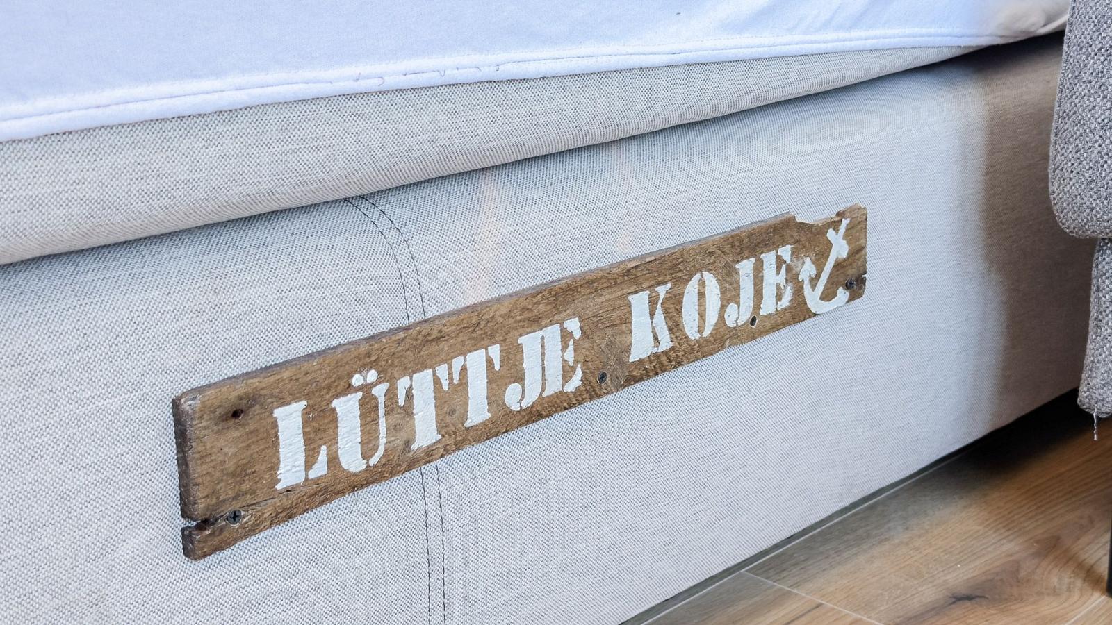 Ein Bett mit einem Holzschild, das LÜTTE KOJE schreibt.