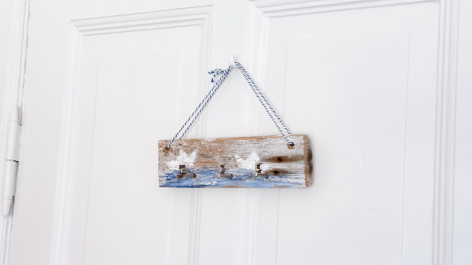 Holz-Hakenplatte mit blau-weißem Seil hängt an einer weißen Tür.
