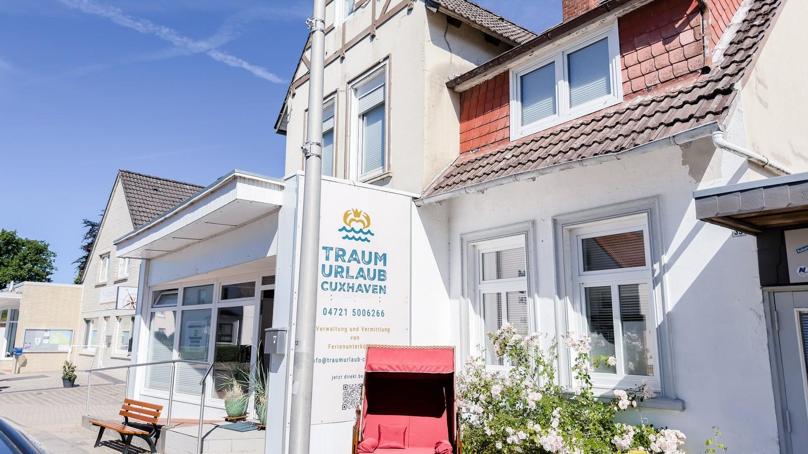 Ferienhaus mit rotem Schirm und Blumen vor einem weißen Gebäude.