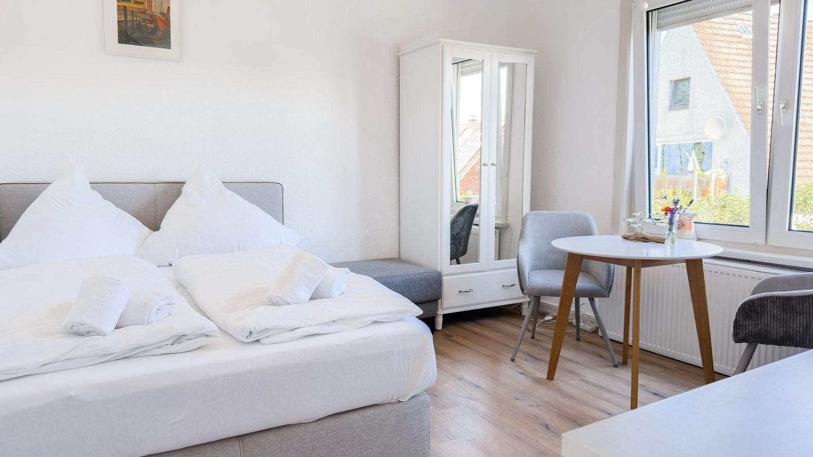 Schlafzimmer mit Bett, Kleiderschrank und Tisch. Fensterblick auf Dach und Garten.