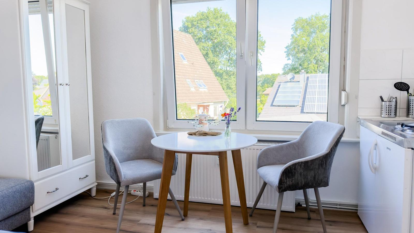 Kleiner Essbereich mit Tisch, zwei Stühlen und Blick auf Dächer und Bäume.