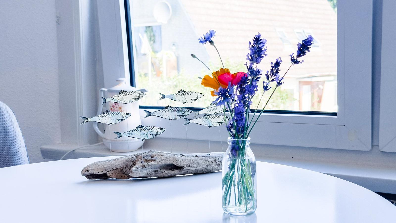 Auf dem Tisch steht eine Vase mit Blumen und ein Fischschwarm-Objekt neben einem Holzstück.