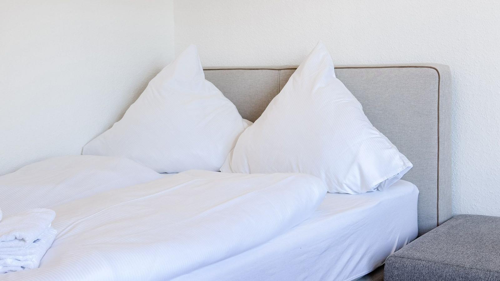 Ein Bett mit weißer Bettwäsche und zwei Kissen. An der Wand ist ein grauer Kopfteil.