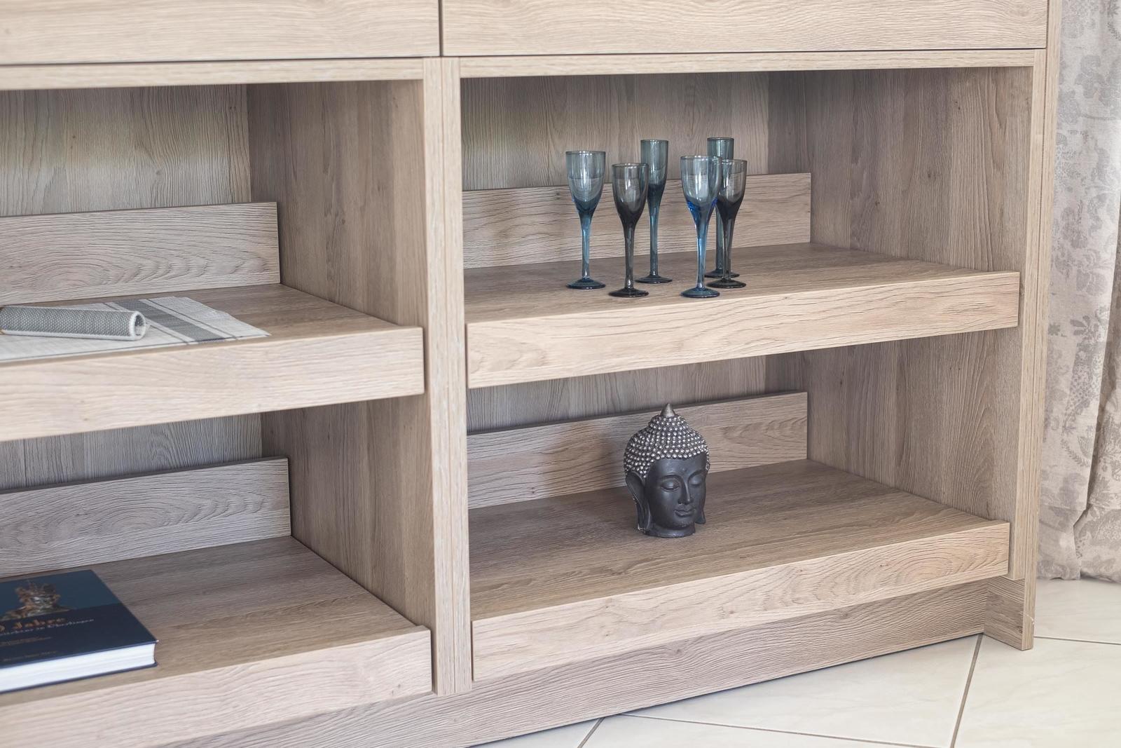 Holzregal mit Gläsern und Buddha-Statue auf den Regalen.