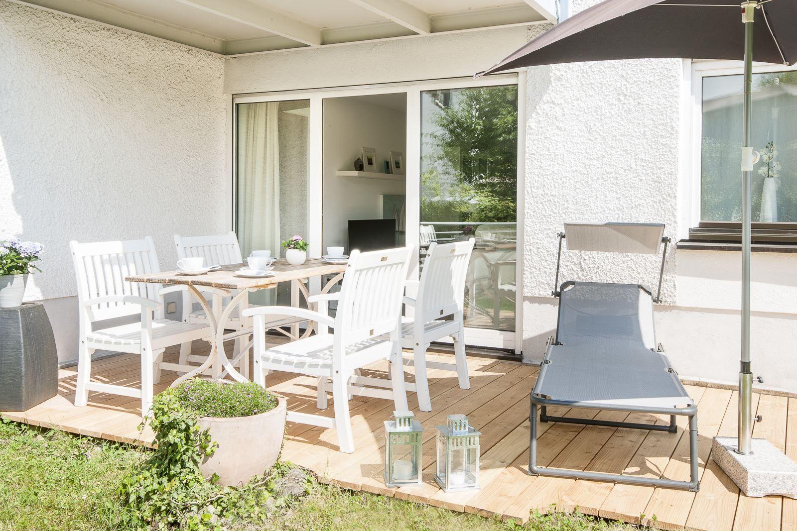 Terrasse mit Esstisch, Stühlen und Liegestuhl unter Sonnenschirm.