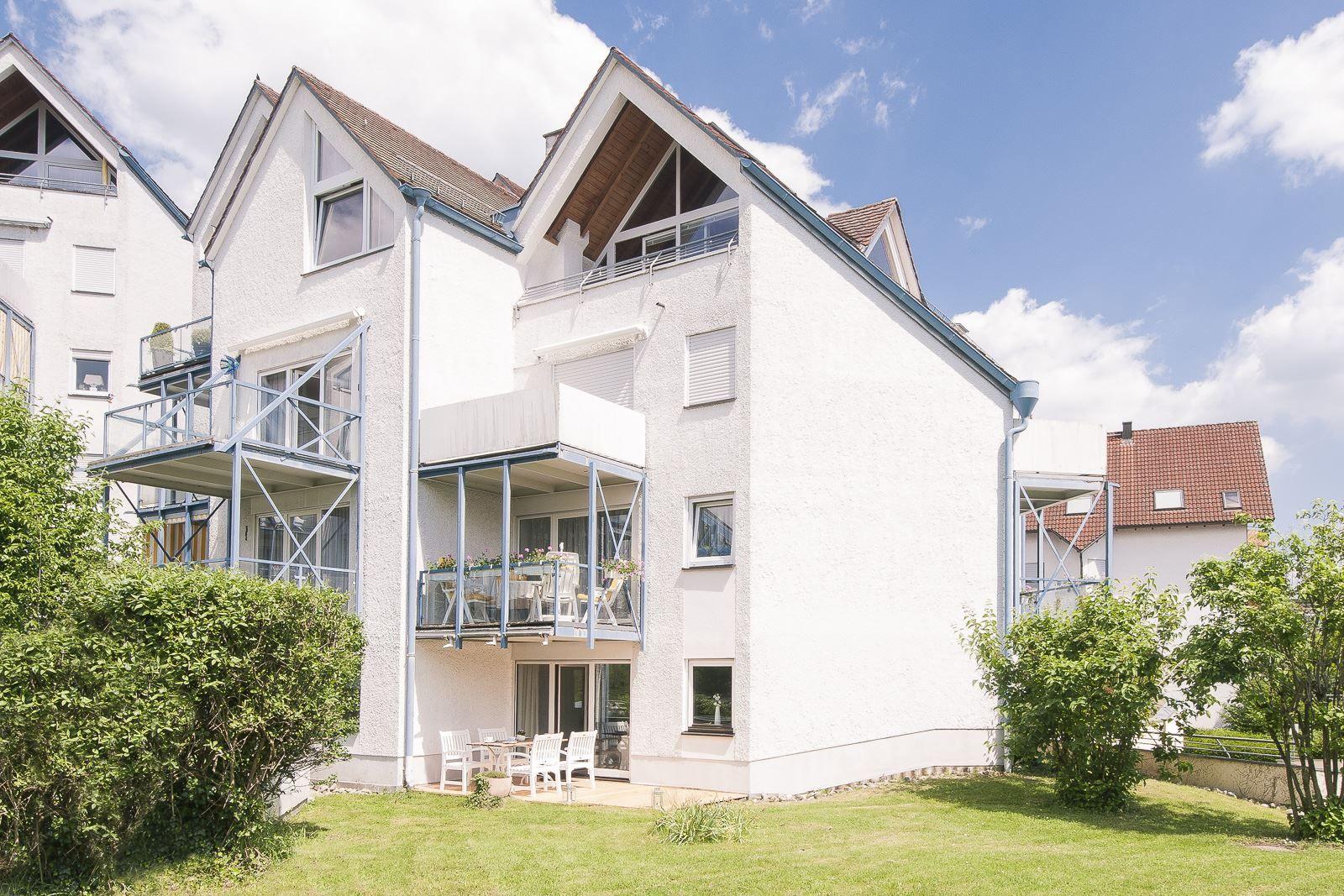 Wohnhaus mit Balkonen und Garten. Weiße Fassade, blauer Himmel.