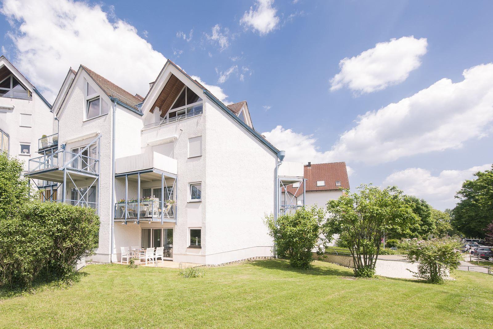 Weiße Mehrfamilienhaus mit Balkonen und grünem Rasen unter blauem Himmel.