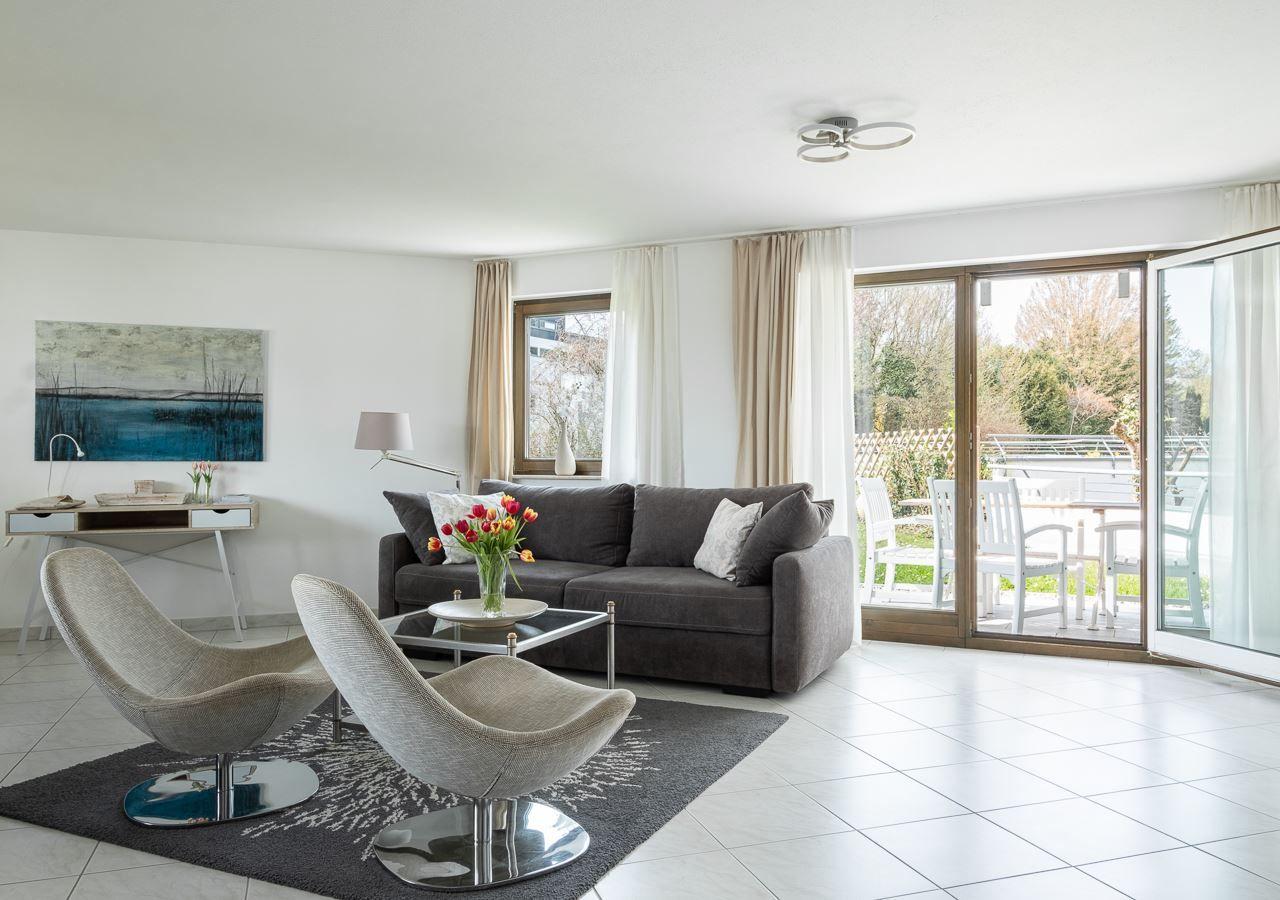 Wohnzimmer mit grauem Sofa, zwei Stühlen und Blick auf Terrasse.