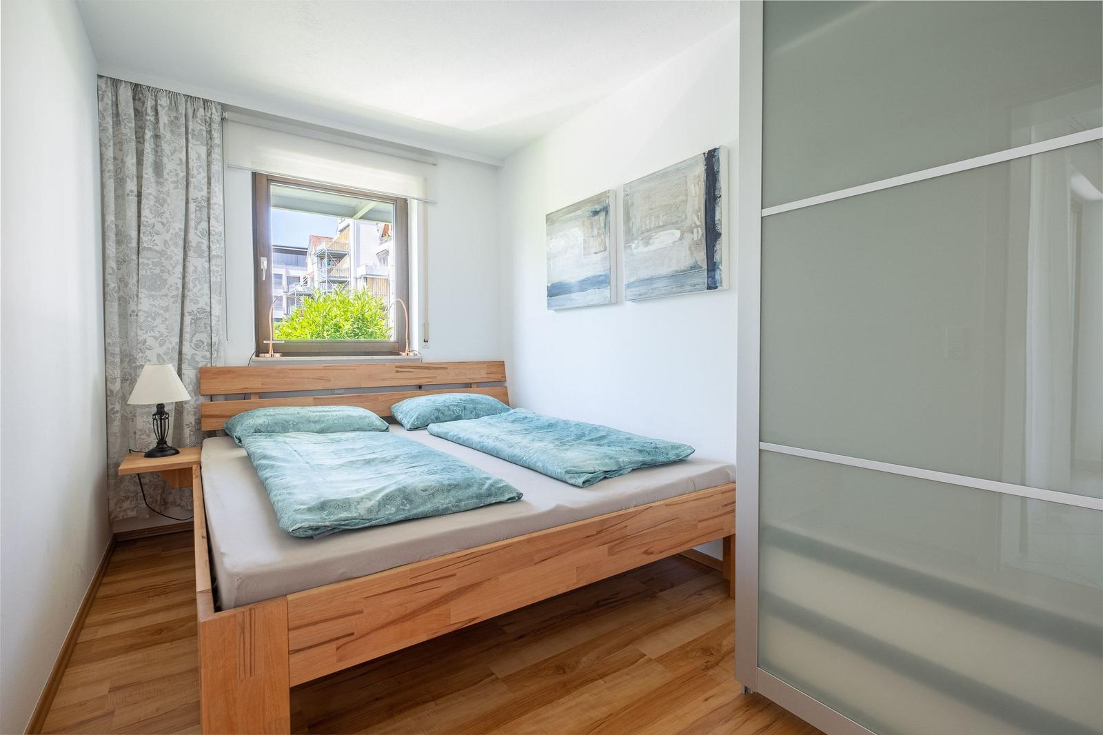 Schlafzimmer mit Holzbett, Fenster und Kleiderschrank.