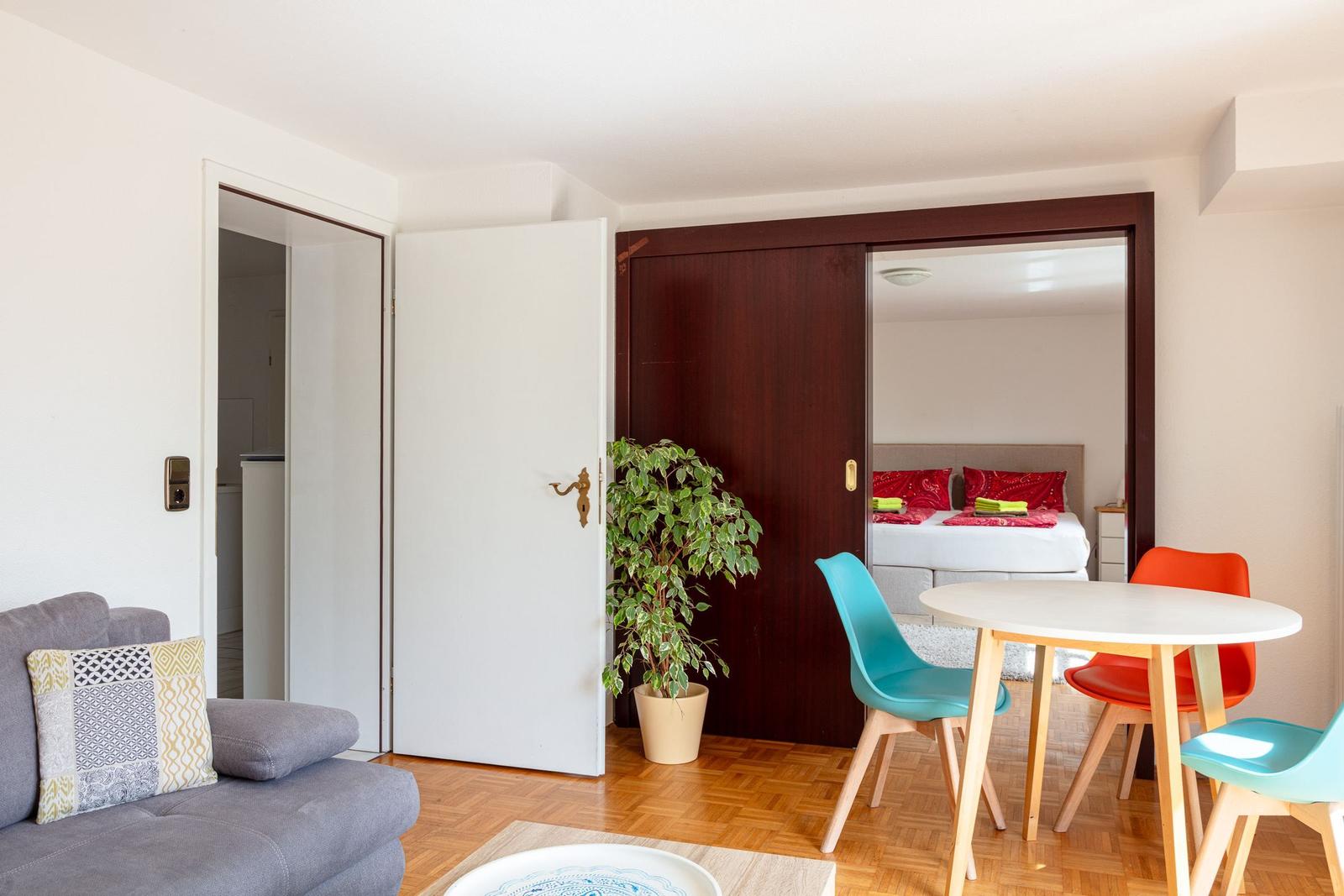 Wohnbereich mit Sofa, Esstisch und Blick in Schlafzimmer mit Bett.