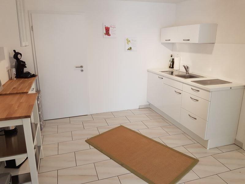 Küche mit weißen Schränken, Arbeitsplatte und Spüle. Holztisch und Teppichboden.
