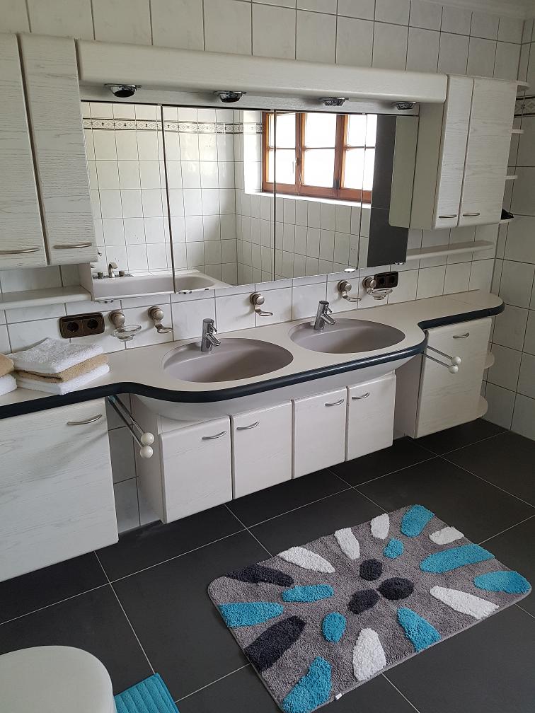 Badezimmer mit zwei Waschbecken, Spiegelschrank und buntem Teppich auf dunklem Boden.