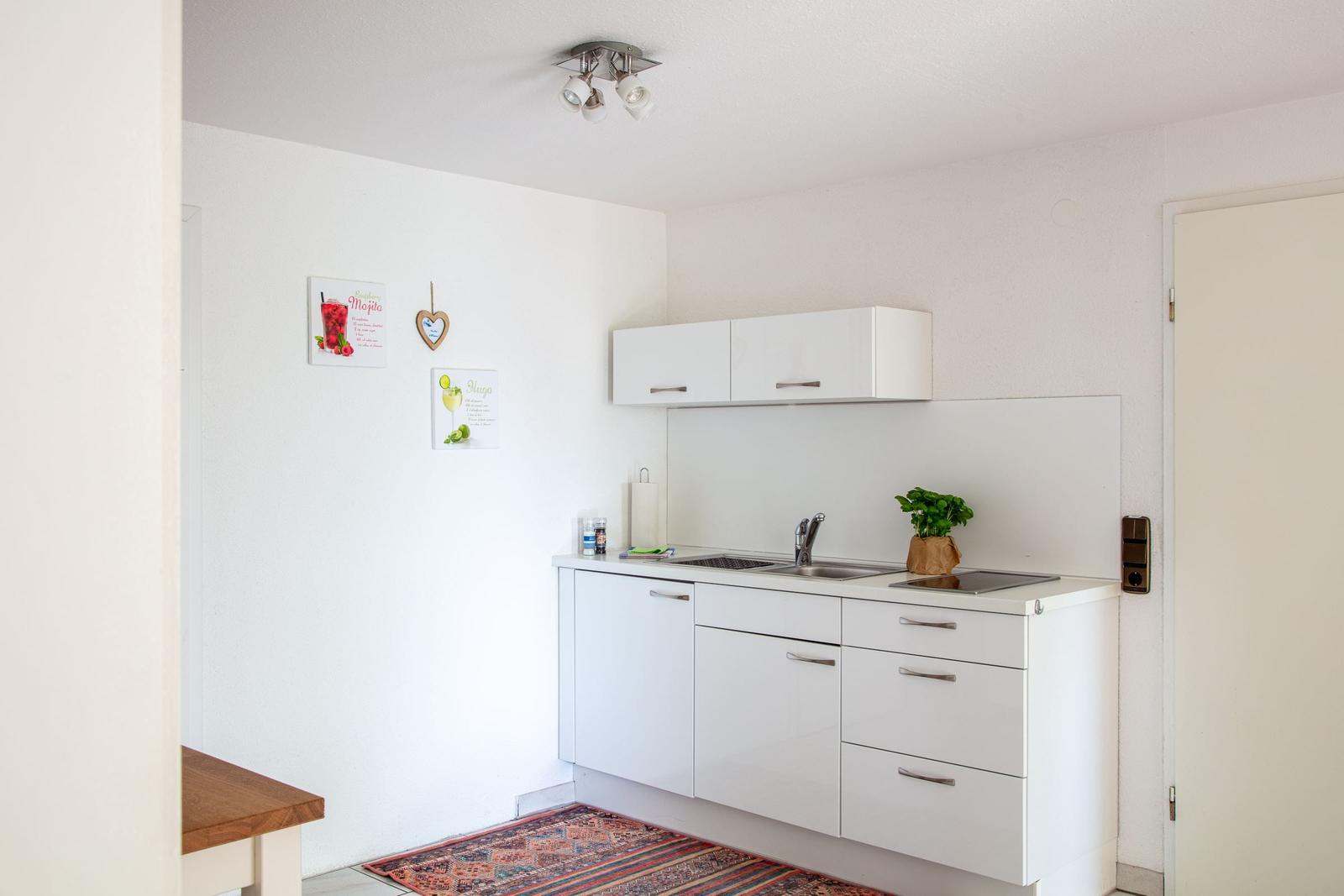 Küche mit weißen Schränken, Spüle und Kochfeld. Wandbild und Teppich sind sichtbar.