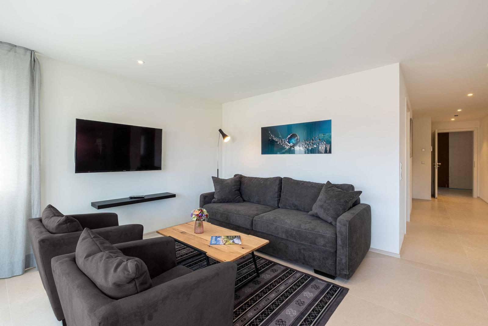 Wohnzimmer mit Sofa, Sessel, Couchtisch und Wandbild. Fernseher an der Wand.