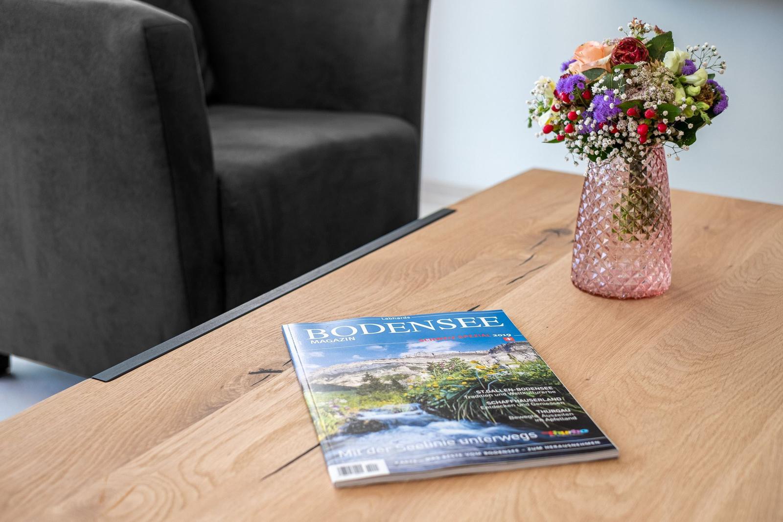 Auf dem Tisch liegt eine Zeitschrift und ein Blumenstrauß in einem Vasen.