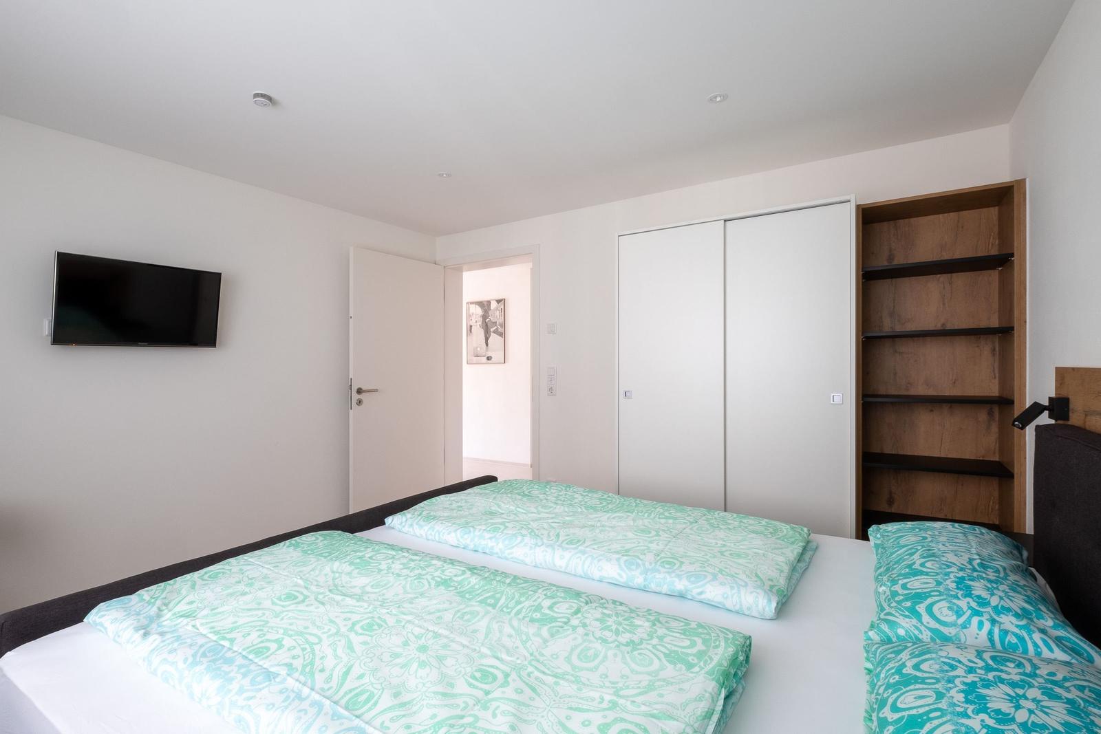 Schlafzimmer mit Doppelbett, Schrank und Wandfernseher