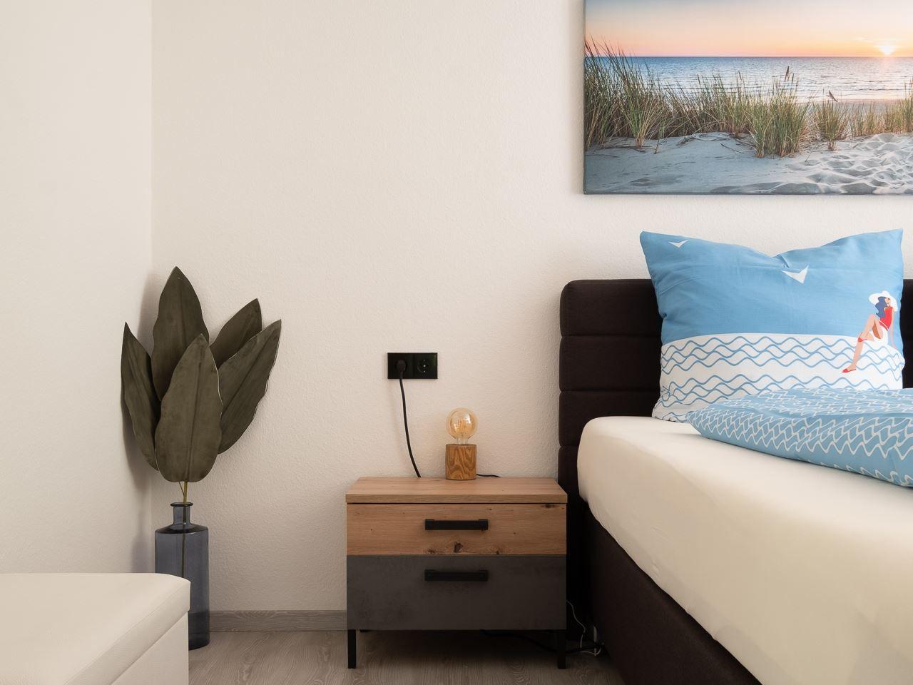 Schlafzimmer mit Bett, Nachttisch und Wandbild. Dekorative Pflanze und Lampen.