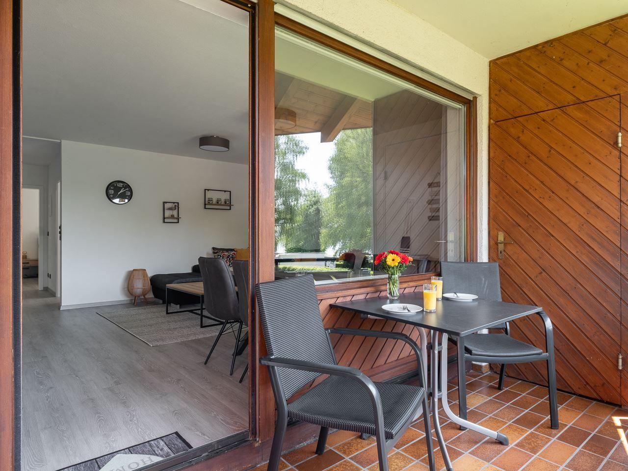 Terrasse mit Tisch und Stühlen, Blick in Wohnzimmer mit Sofa und Wanduhr.