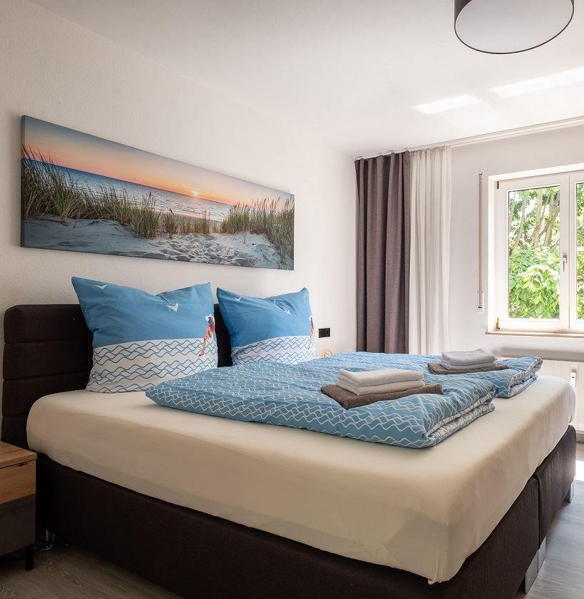 Schlafzimmer mit Bett, Wandbild und Fenster mit Blick auf Grün.