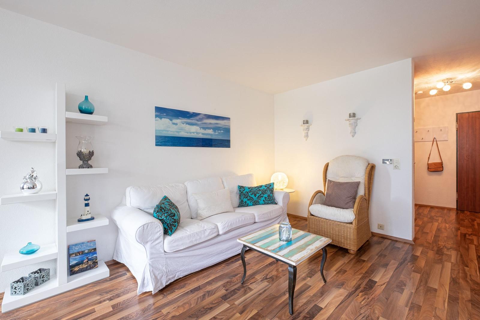 Wohnzimmer mit Sofa, Sessel und Holzboden. Wandbild und Regal mit Dekoration.