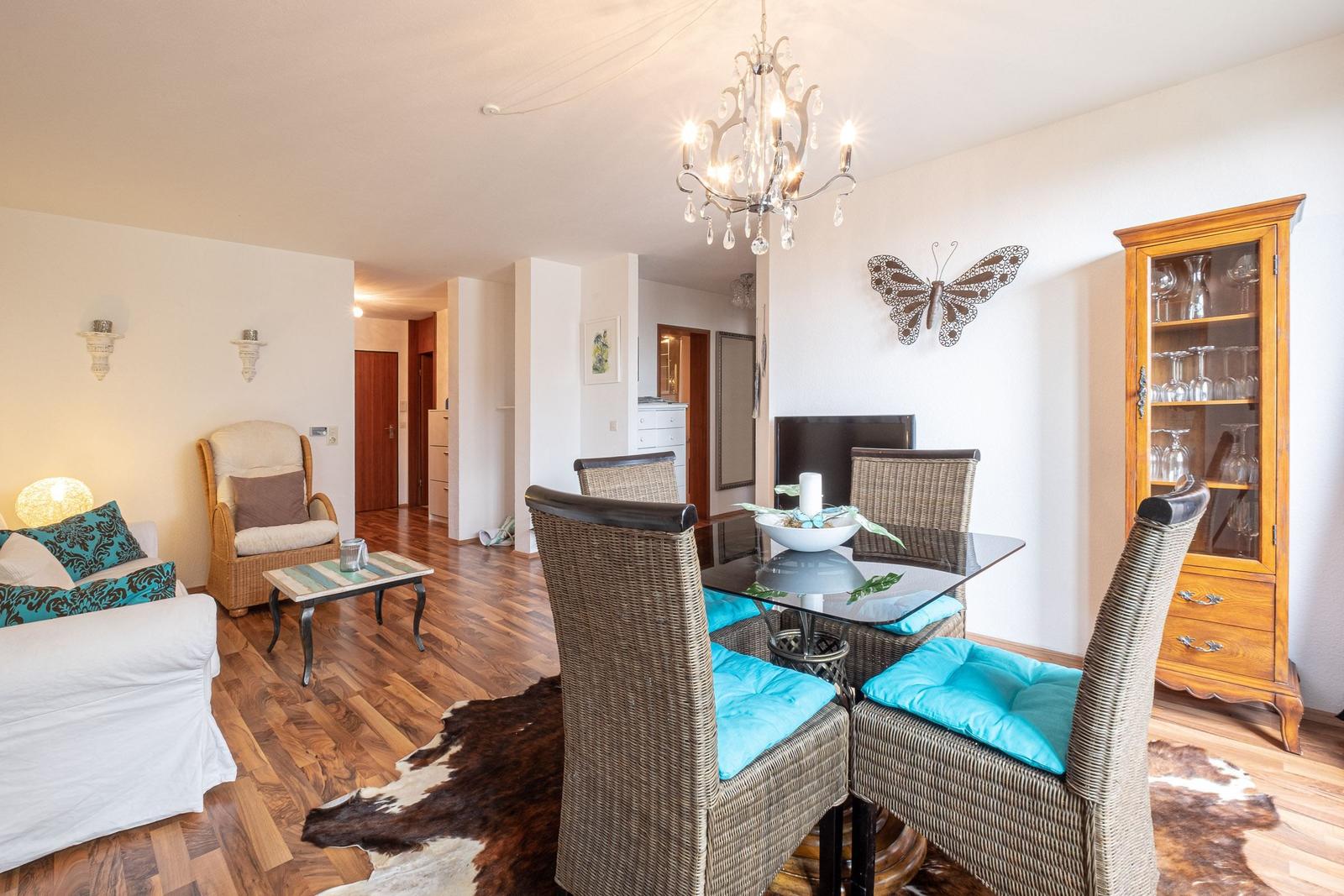 Essbereich mit Glasplatte und Stühlen mit türkisen Kissen. Wohnbereich mit Sofa und Esstisch.
