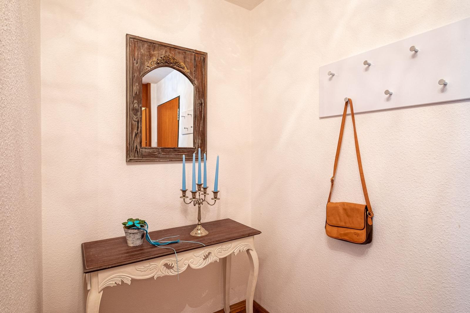 Hausflur mit Spiegel, Tisch, Kerzen und Handtasche an Wandhalterung.