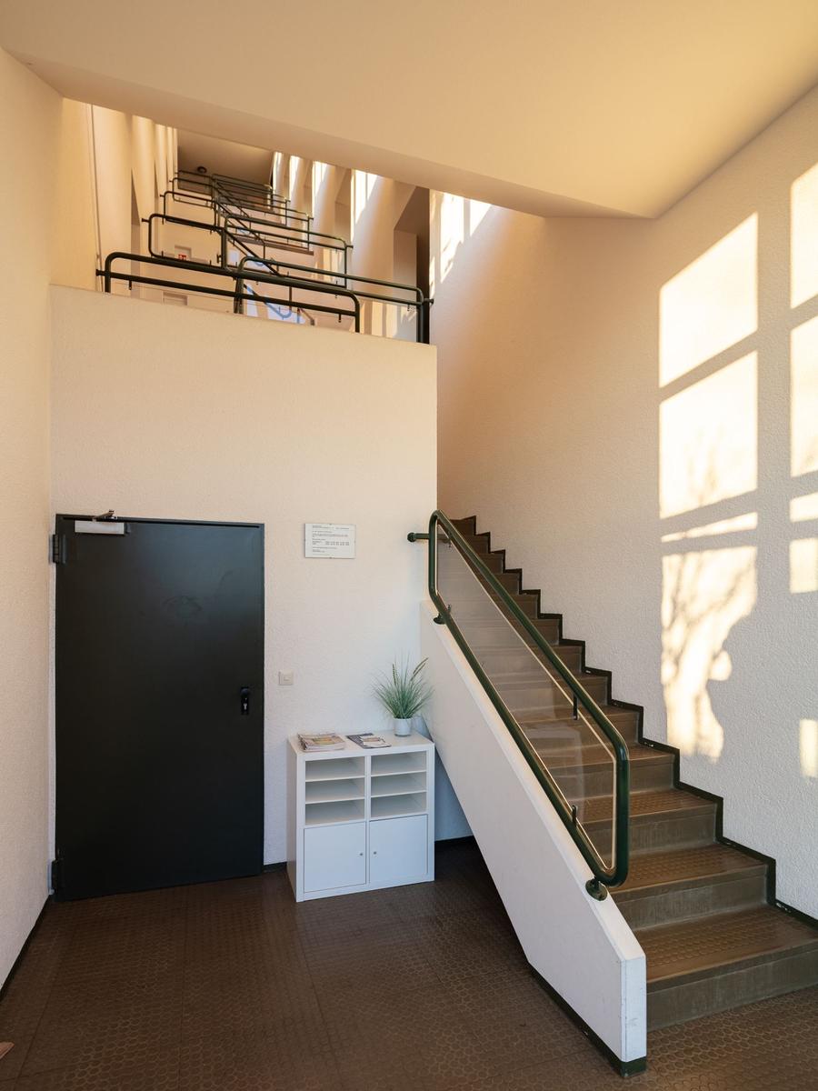 Treppe mit Glasgeländer führt zur oberen Etage. Schwarze Tür und weißer Schrank stehen im Flur.