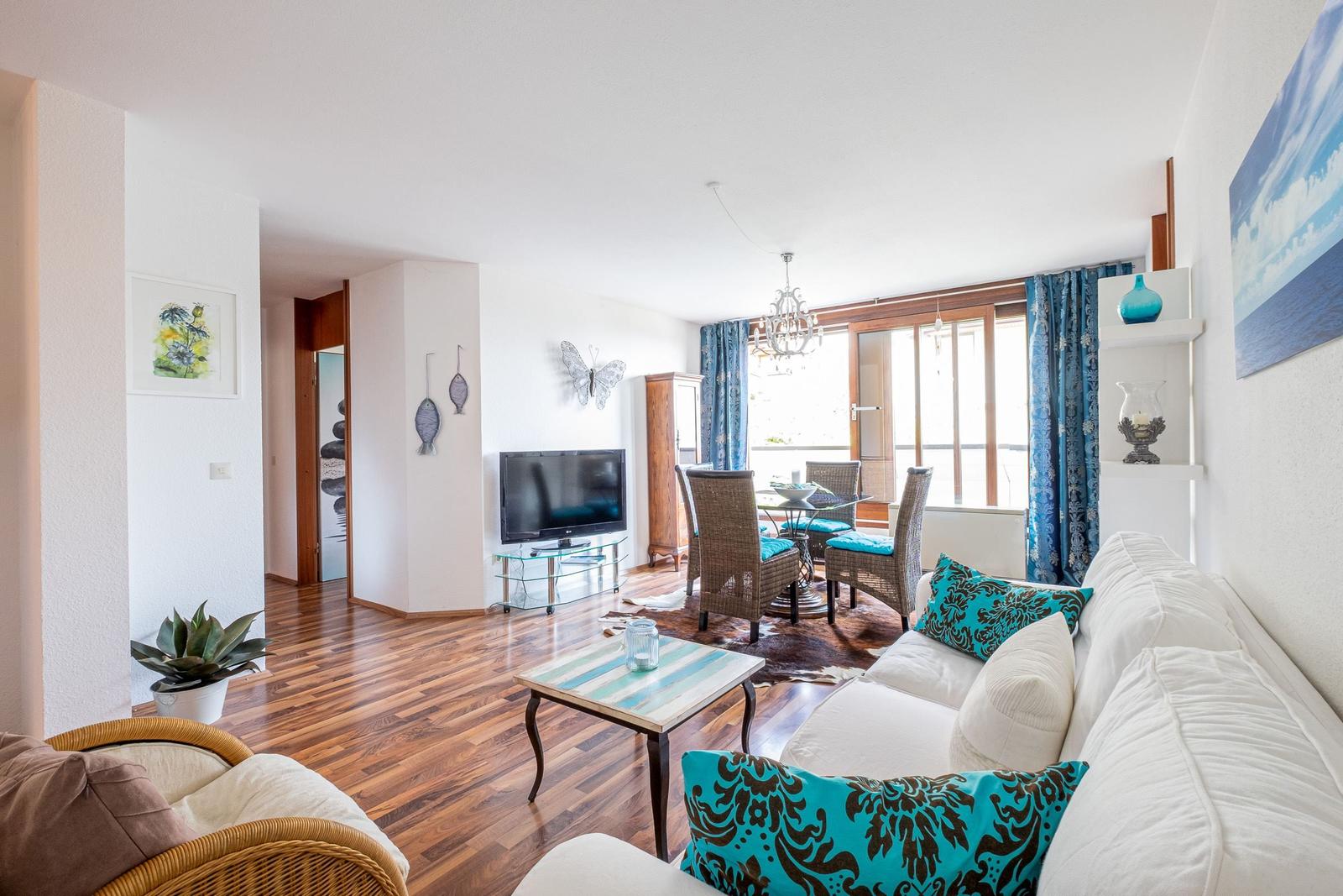 Wohn- und Essbereich mit Sofa, TV und Terrassentür.