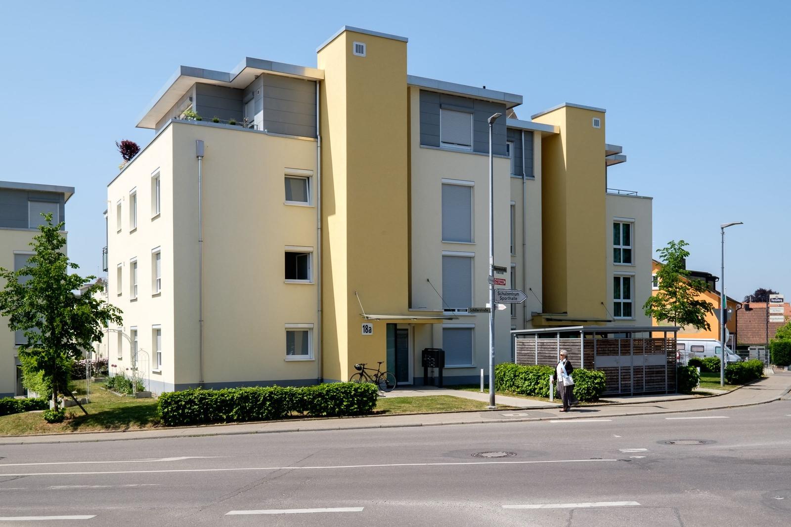 Moderne Wohnhausfassade mit gelben und grauen Akzenten, Eingangsbereich und Fahrrad.