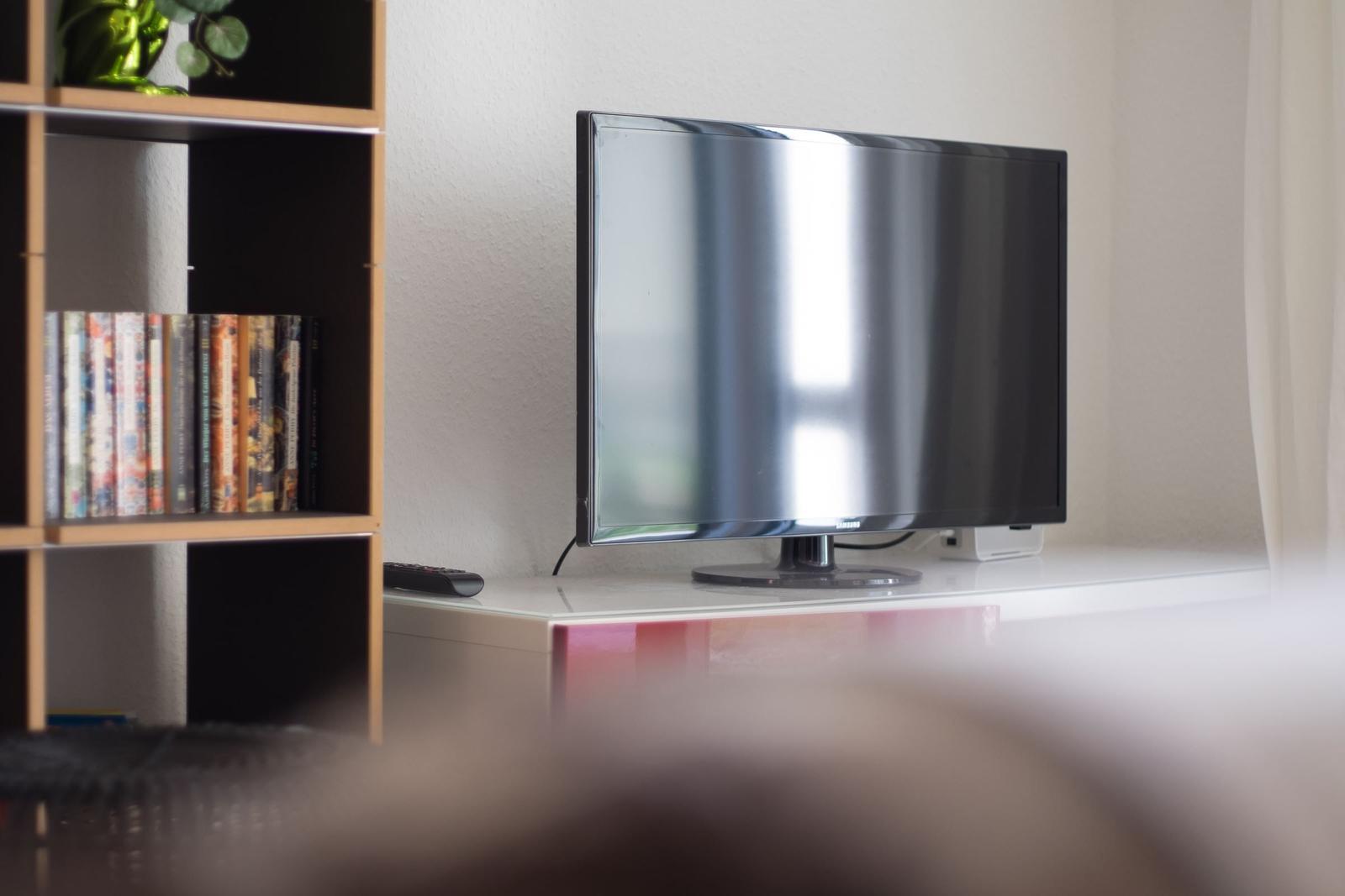 Flachbildfernseher auf weißem Möbelstück neben Bücherregal mit DVDs.