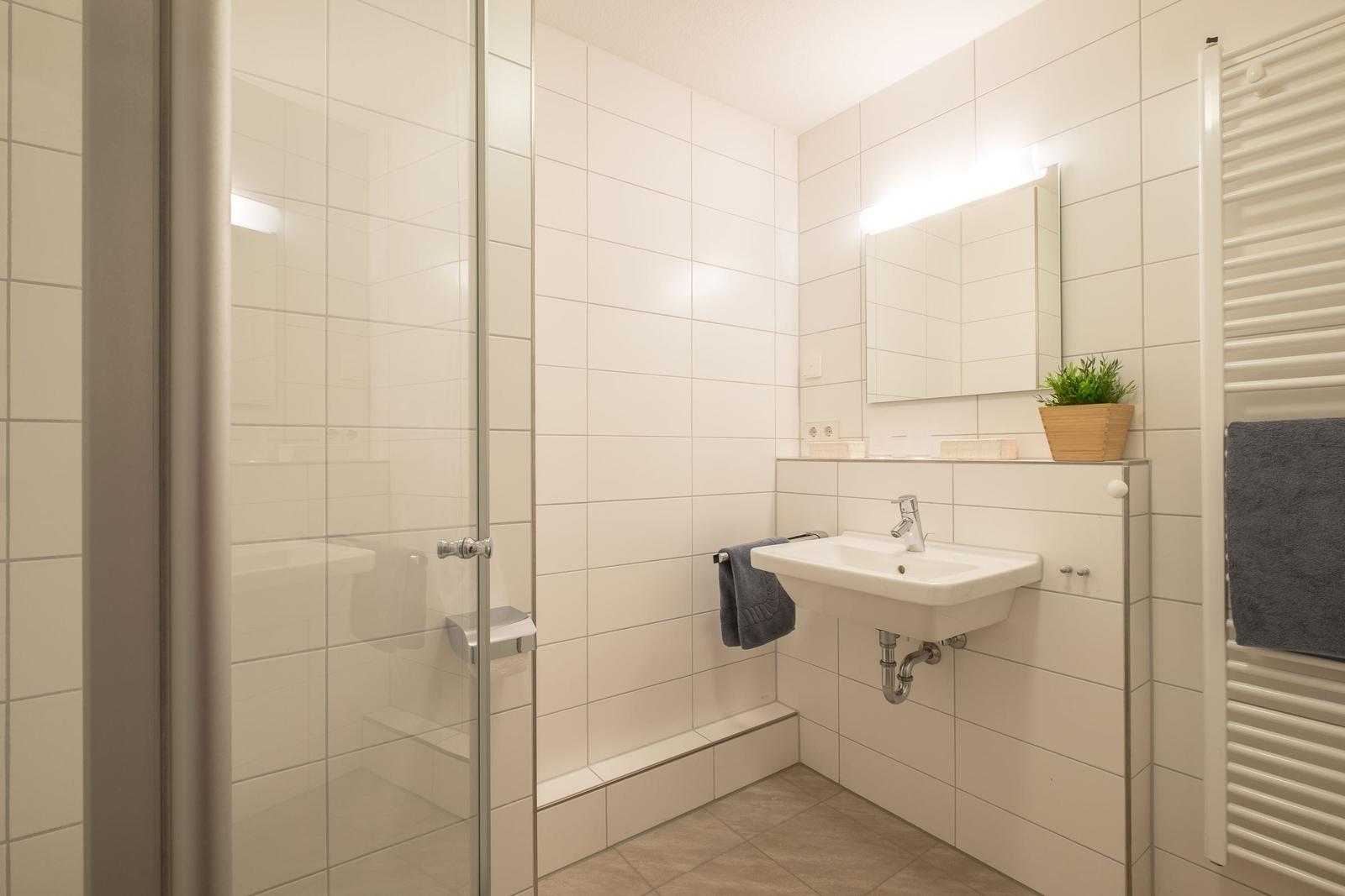 Badezimmer mit Dusche, Waschbecken und Heizkörper